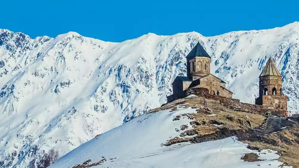 De Gergeti Trinity Church boven Kazbegi met besneeuwde Kaukasus-toppen erachter