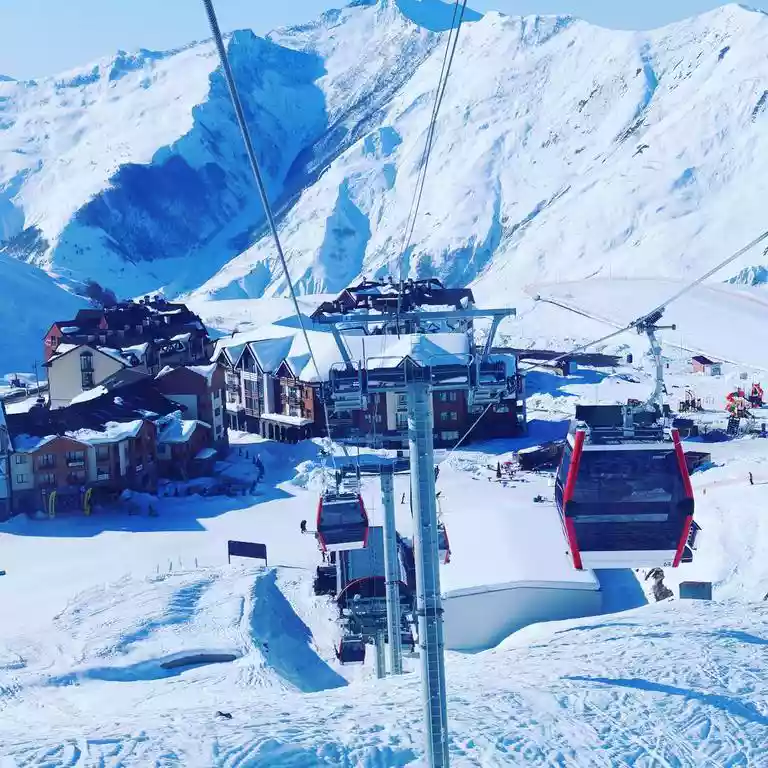 Een gondel met rode cabines boven de chalets van Gudauri