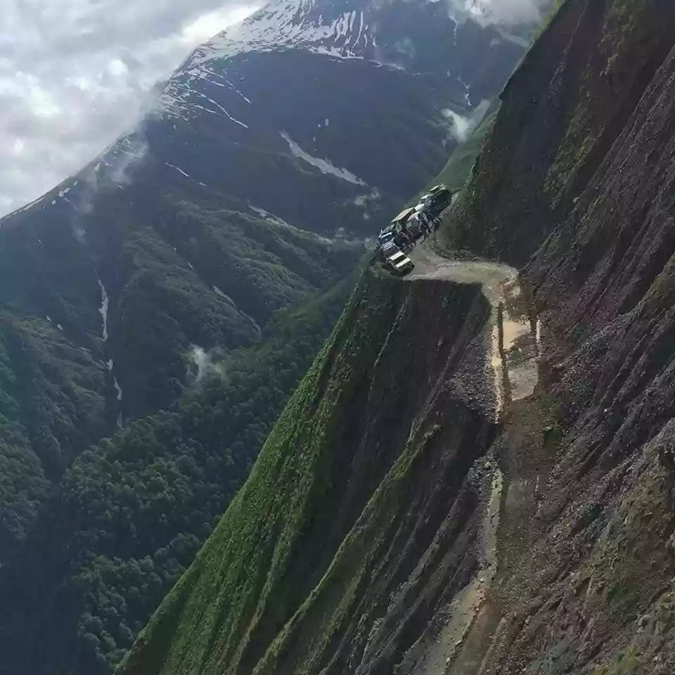 Terreinwagens op de smalle onverharde bergweg naar Toesjeti, hoog boven een beboste afgrond