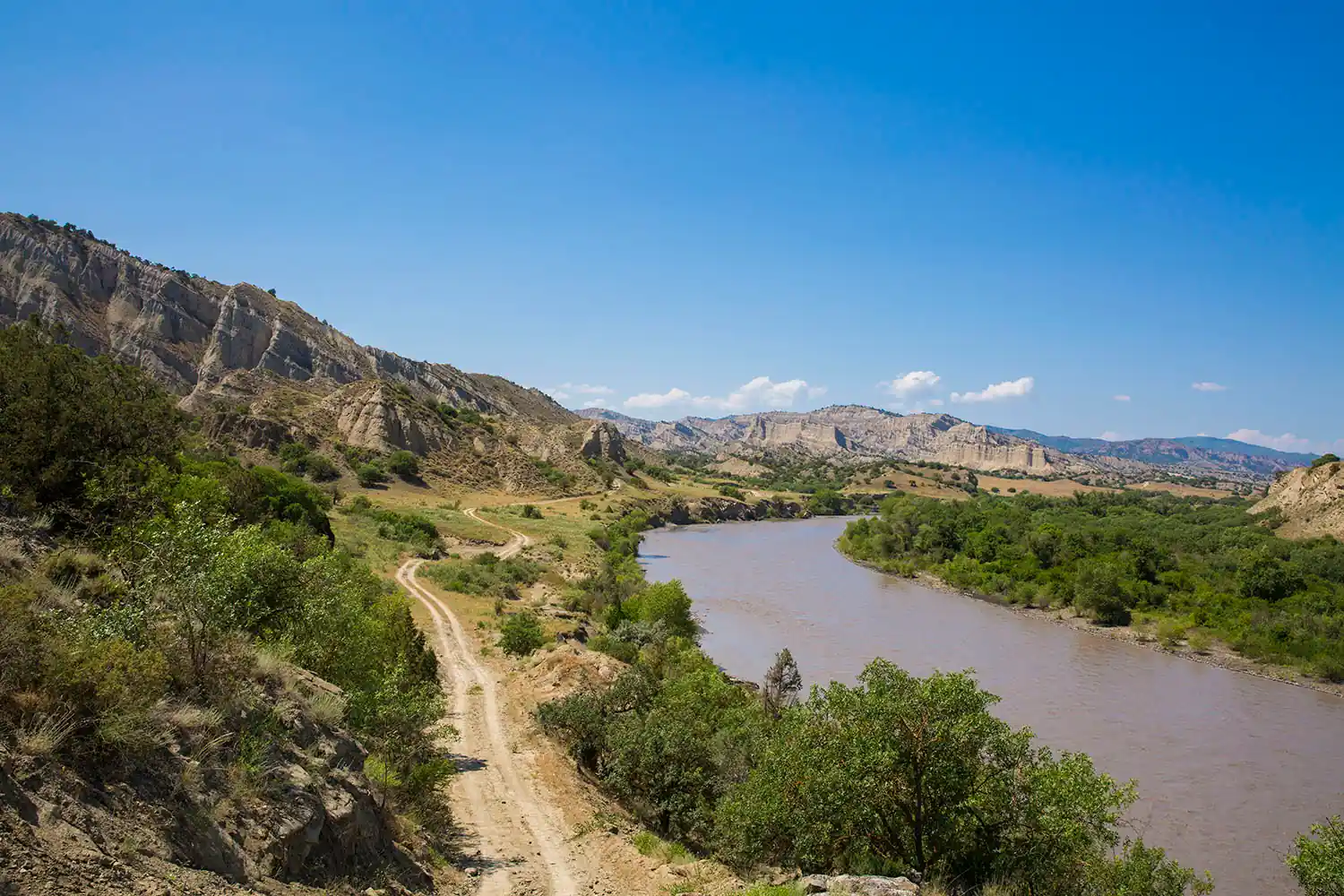Onverharde weg langs de Alazani tussen de geërodeerde kleiruggen van Nationaal Park Vashlovani, Georgië