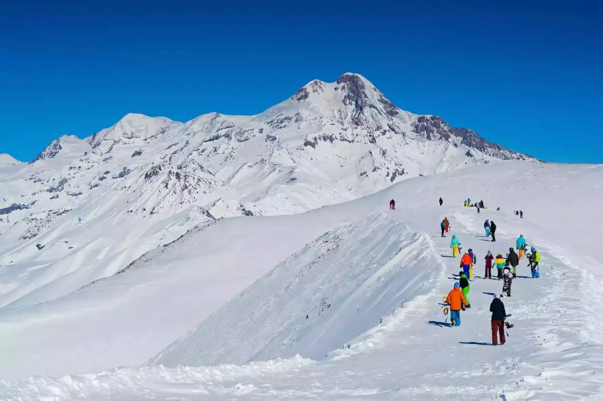 Skiërs lopen over een besneeuwde rug onder een brede bergtop in de Kaukasus bij Gudauri
